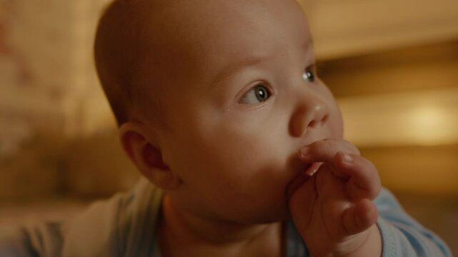 Portrait of a cute baby with a finger in his mouth looking aside. The concept of caring for a newborn. Parenting. The concept of motherhood.