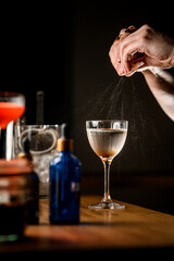 Focus on a glass of clear liquid, over which female hands of a bartender squeeze a piece of zest