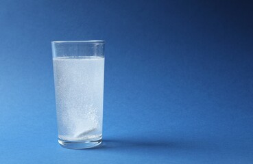 Effervescent pill dissolving in a glas water on blue background 