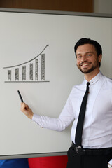 A man is standing in front of a white board with a graph drawn on it. He is smiling and holding a...