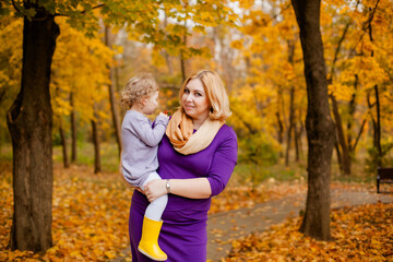 Fototapeta premium Plus-size woman in purple dress holding and playing with her 3-year-old daughter in autumn park
