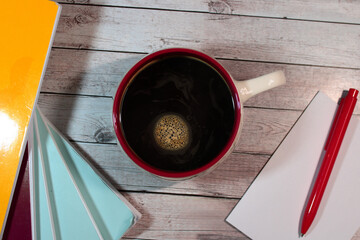 A warm, cozy scene with a top-down view of a red-rimmed coffee mug filled with black coffee, placed on a rustic wooden surface. 