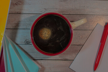 A warm, cozy scene with a top-down view of a red-rimmed coffee mug filled with black coffee, placed on a rustic wooden surface. 
