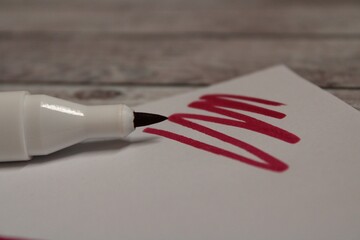 Red Marker on a white sheet of paper on a wooden background