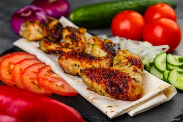 Delicious hot grill  kebab from chicken with vegetables, served on a slate plate close-up on a table.
