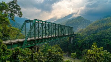 Obraz premium A green metal bridge spans a valley with lush green mountains in the background.
