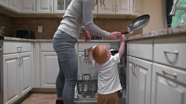 toddler reaches into open dishwasher in kitchen, unsupervised. moment potential risks of children interfering with household appliances, importance of kitchen safety supervision to prevent accidents - Powered by Adobe