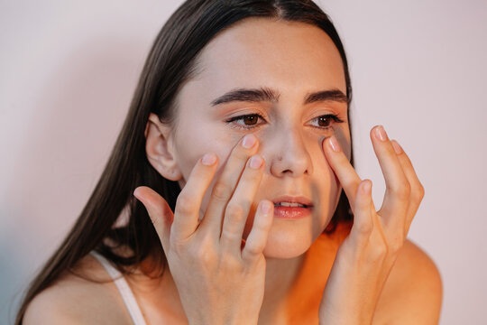 Close-up of a young Woman dabbing eye cream on her lower eyelids with her middle and ring fingers