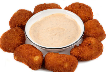 A plate of fried chicken nuggets with a dipping sauce. The sauce is a creamy white color