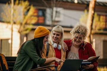 Three multiracial college students are sitting outside and working on a group project together.
