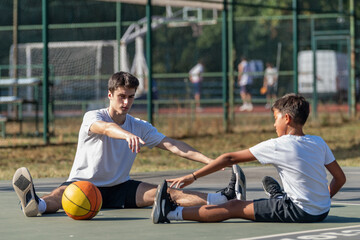 Obraz premium Young boy stretches with his coach during basketball training, focusing on flexibility and preparation. This outdoor session highlights foundational skills and active, healthy habits for youth.