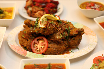 Fried chicken garnished with fresh herbs and lemon slices is served alongside colorful bowls of various sauces and traditional sides.