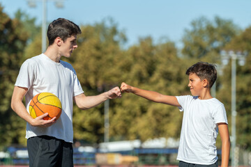 Coach and young boy share a motivating fist bump during outdoor basketball training. This teamwork moment highlights sportsmanship, encouragement, and active engagement in youth sports.