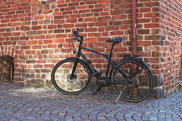 Modern black bicycle parked next to an old red brick building.