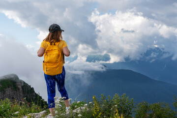 woman hiker with a yellow backpack in a cap walking in the mountains against the background of clouds Picturesque mountain landscape Active lifestyle copy space