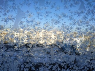Snowflakes on window frost on glass city view background blue sky brightly lit houses yellow light New Year Christmas frosty natural pattern on winter window ice pattern with sunlight winter panorama