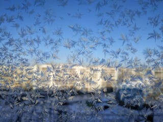 Snowflakes on window frost on glass city view background blue sky brightly lit houses yellow light New Year Christmas frosty natural pattern on winter window ice pattern with sunlight winter panorama