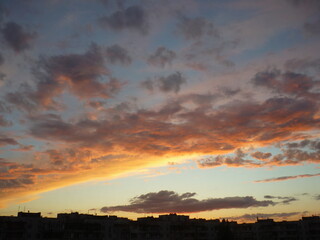 Bright unusual sunset city landscape orange pink rays above cityscape. Brutalist panel buildings appear as black silhouettes against a fiery orange-yellow sky dramatic lighting dark rain storm clouds