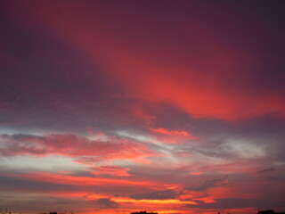 Bright unusual sunset city landscape orange pink rays above cityscape. Brutalist panel buildings appear as black silhouettes against a fiery orange-yellow sky dramatic lighting dark rain storm clouds