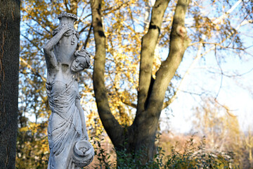 sculpture of a girl in the autumn park. An old statue in a park of a sensual semi-nude Greek or Italian Renaissance woman with a vase in a city park. sunny day in the spring garden. close-up