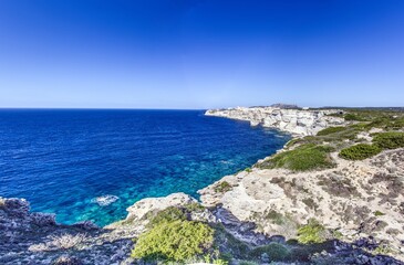 Historic Bonifacio on Corsica’s dramatic limestone cliffs against a clear blue Mediterranean sea and sky