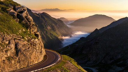 Overlooking a winding mountain road at dawn, with steep cliffs on both sides and distant peaks disappearing into morning fog