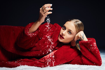 Naklejka premium Young beautiful woman in a striking red coat gracefully playing with snow indoors