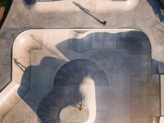 Aerial view of a modern skateboard park featuring diverse ramps and a skater performing tricks in the afternoon light