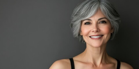 Naklejka premium Beautiful smiling senior woman with short gray hair posing against a gray background. Beauty photography.