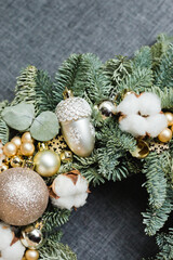 Christmas wreath decorated with cotton, berries and gold balls on a gray background. Hand made work, closeup