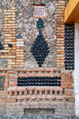 The Bottle House in Ganja, Azerbaijan showcases a decorative design of triangular patterns formed by stacked glass bottles, complemented by a mosaic wall and red bricks