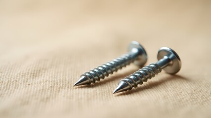 Screws and bolts for furniture repair. Two metal screws lie on a light surface, showcasing their shiny appearance. Both screws have pointed tips and smooth threads.