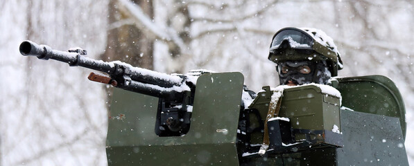 Soldier aiming a machine gun from an armored vehicle during a military operation in the snow.