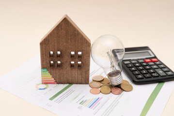 Electricity bill with wooden house model, light bulb, several coins and calculator on neutral background. Concept of electricity prices and tax payments