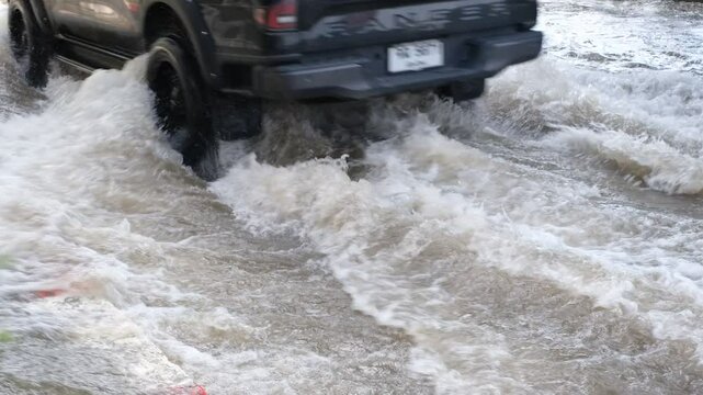 A car is driving through a flooded street. The water is murky and the car is barely visible