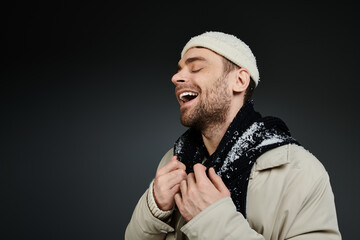 Joyful young man in a winter coat laughing warmly against a dark background