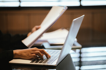 Fototapeta premium Young Asian businesswoman pointing pen with graph and chart report and using laptop computer to analyze data.