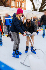 Young adult attractive beautiful caucasian woman enjoy having fun with little toddler son at outdoor skating rink while travel old european city in winter. Mom and child holiday sport activities