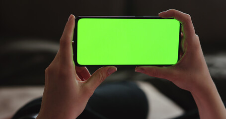 Young woman lying on a couch and using smartphone with horizontal green screen