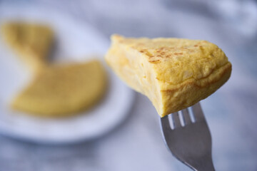 Bite of a potato omelette (Spanish tortilla) stuck on a fork. Typical tapas and rations of Spanish cuisine.