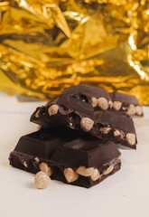 broken dark chocolate bar with hazelnuts on white backdrop, glowy golden background.top view of luxury desert, slabs one over another.empty space for text on box.