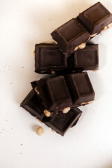broken dark chocolate bar with hazelnuts on white backdrop, glowy golden background.top view of luxury desert, slabs one over another.empty space for text on box.