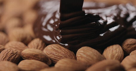 closeup covering roasted almonds with melted dark chocolate