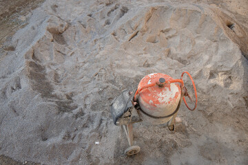 A weathered concrete mixer sits idle on a large pile of sand, indicating a construction or...