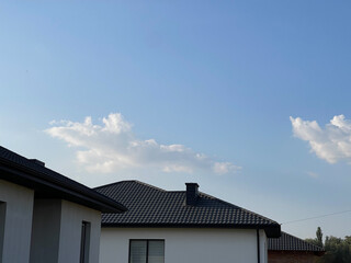 The photo shows a roof made of metal tiles. White house and black roof. Metal chimney.