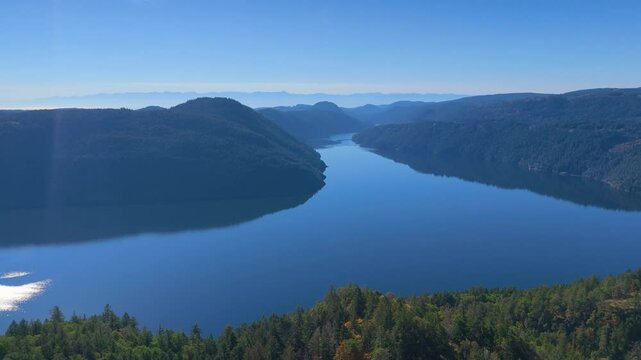 Stunning aerial view of Saanich Inlet surrounded by lush green forests and distant blue mountains under a clear sky