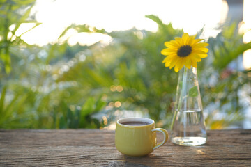 Yellow cup and sunflower in a glass vase on wooden table