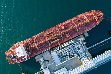 Aerial top down view of a large oil tanker docked at a pier in the port in process of loading.