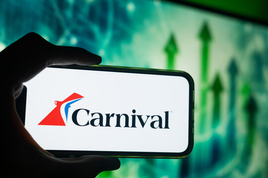 Hand Holding Phone with Carnival (CCL) Logo and Monitor in the Background Showing Green Arrows Pointing Up Suggesting Stock Growth
