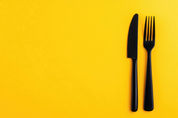 Black fork and knife arranged on a bright yellow background in a minimalistic setting